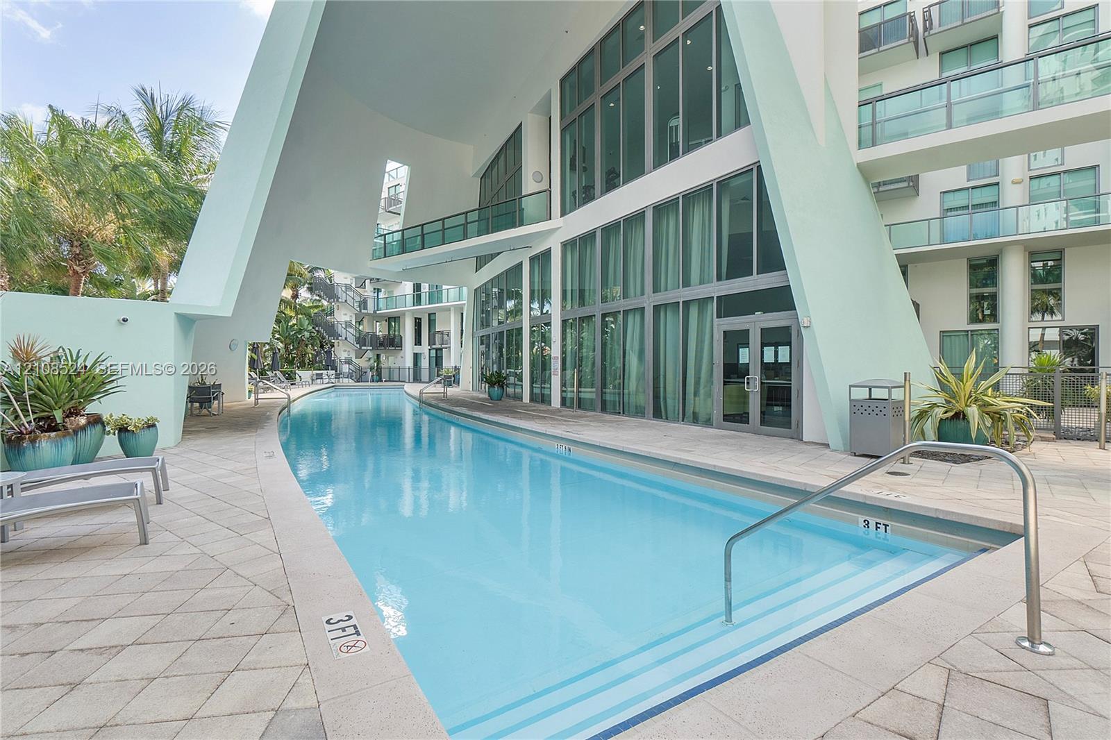 Curved swimming pool featuring paved decking, floor-to-ceiling windows, and angular architectural pillars