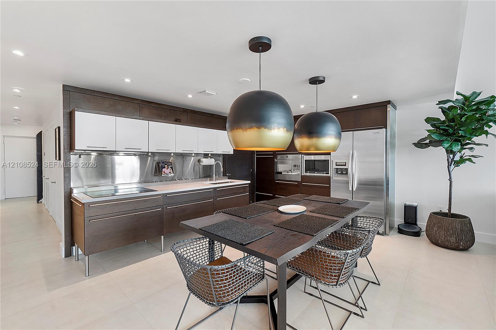 Modern kitchen featuring two-toned cabinetry, stainless steel backsplash, integrated stainless steel appliances, and dual oversized pendant lighting