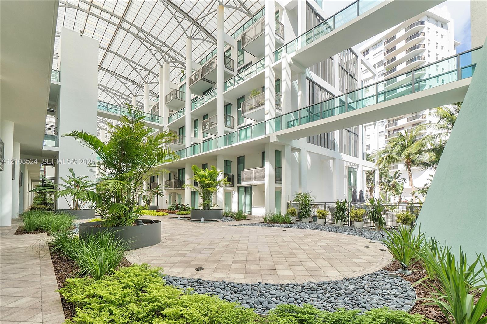 Central atrium featuring a multi-story glass-enclosed canopy, elevated pedestrian bridges, paved hardscaping, and integrated botanical landscaping