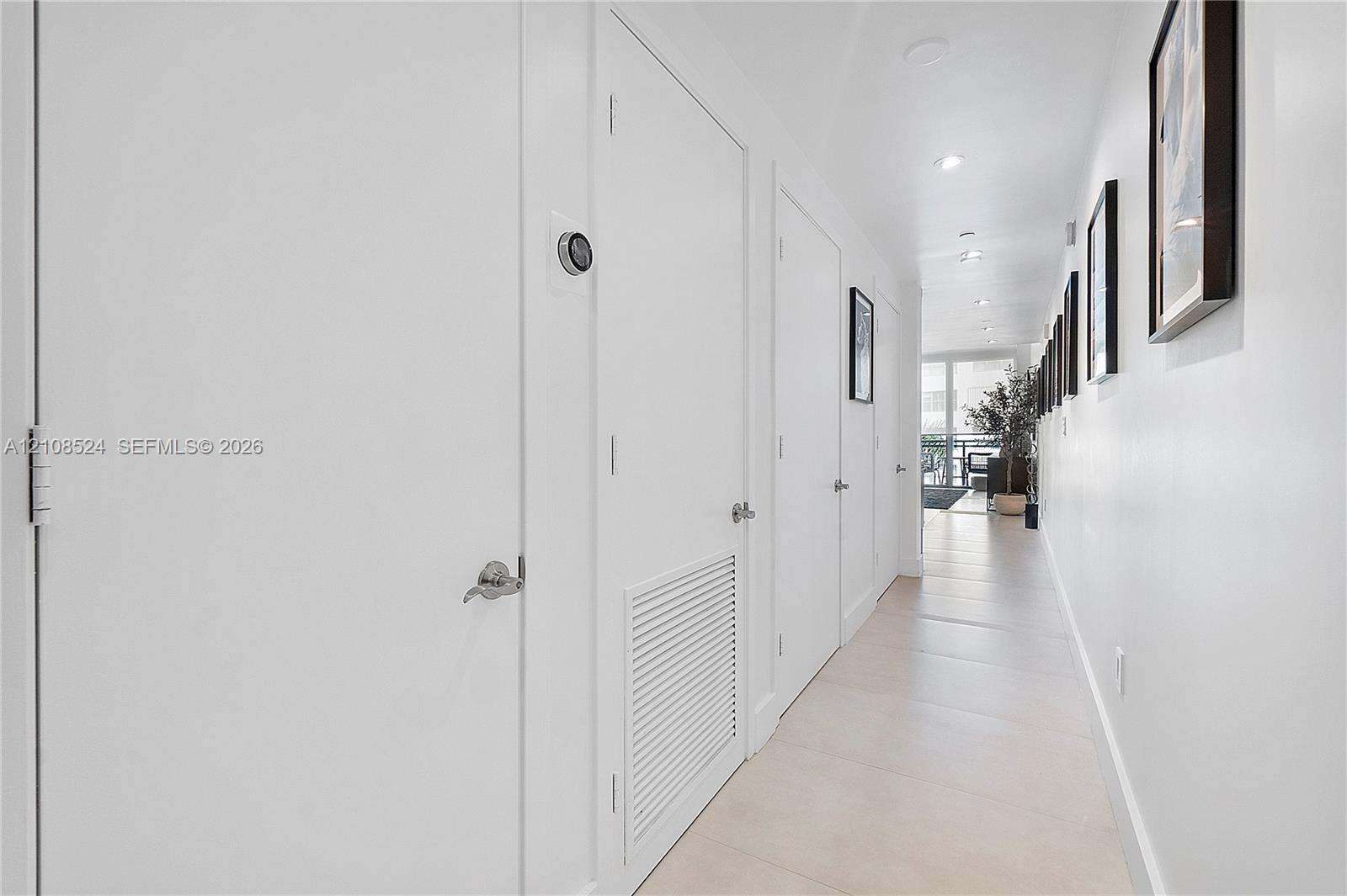 Hallway featuring large-format tile flooring, crisp white walls, recessed ceiling lighting, and multiple interior doors with brushed metal hardware Hallway featuring large-format tile flooring, crisp white walls, recessed ceiling lighting, and multiple interior doors with brushed metal hardware