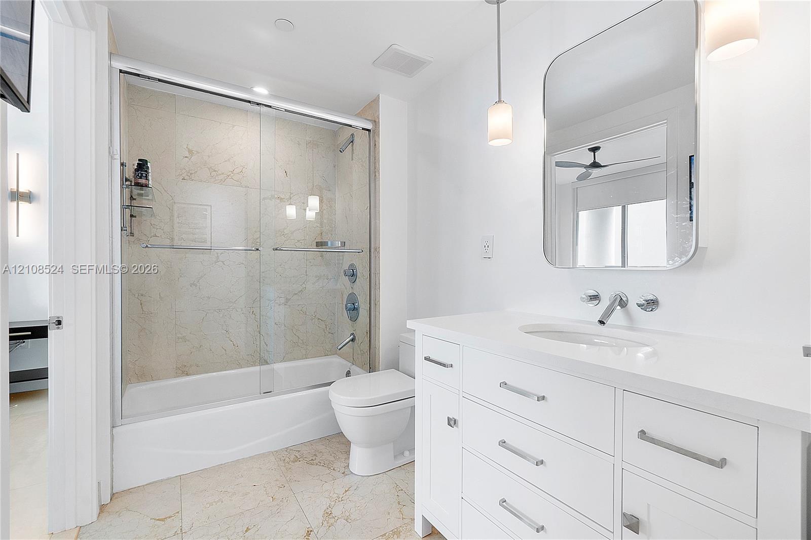Bathroom featuring a white vanity with a solid-surface countertop, an undermount sink with wall-mounted polished chrome hardware, a glass-enclosed shower with full-height stone-finish tile surround, and large-format tile flooring