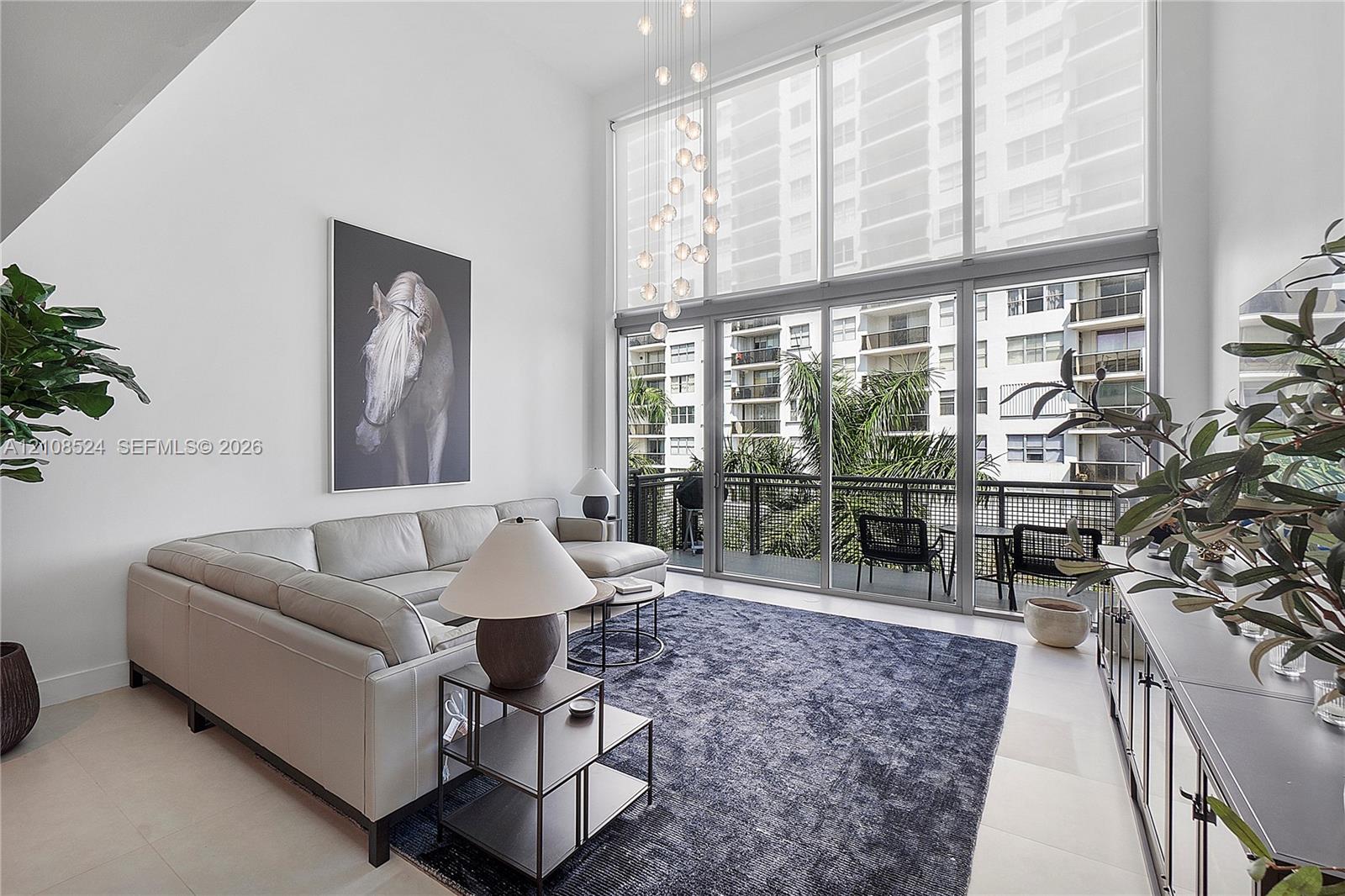Double-height ceilings featuring floor-to-ceiling windows, integrated pendant lighting, and a metal-railed balcony