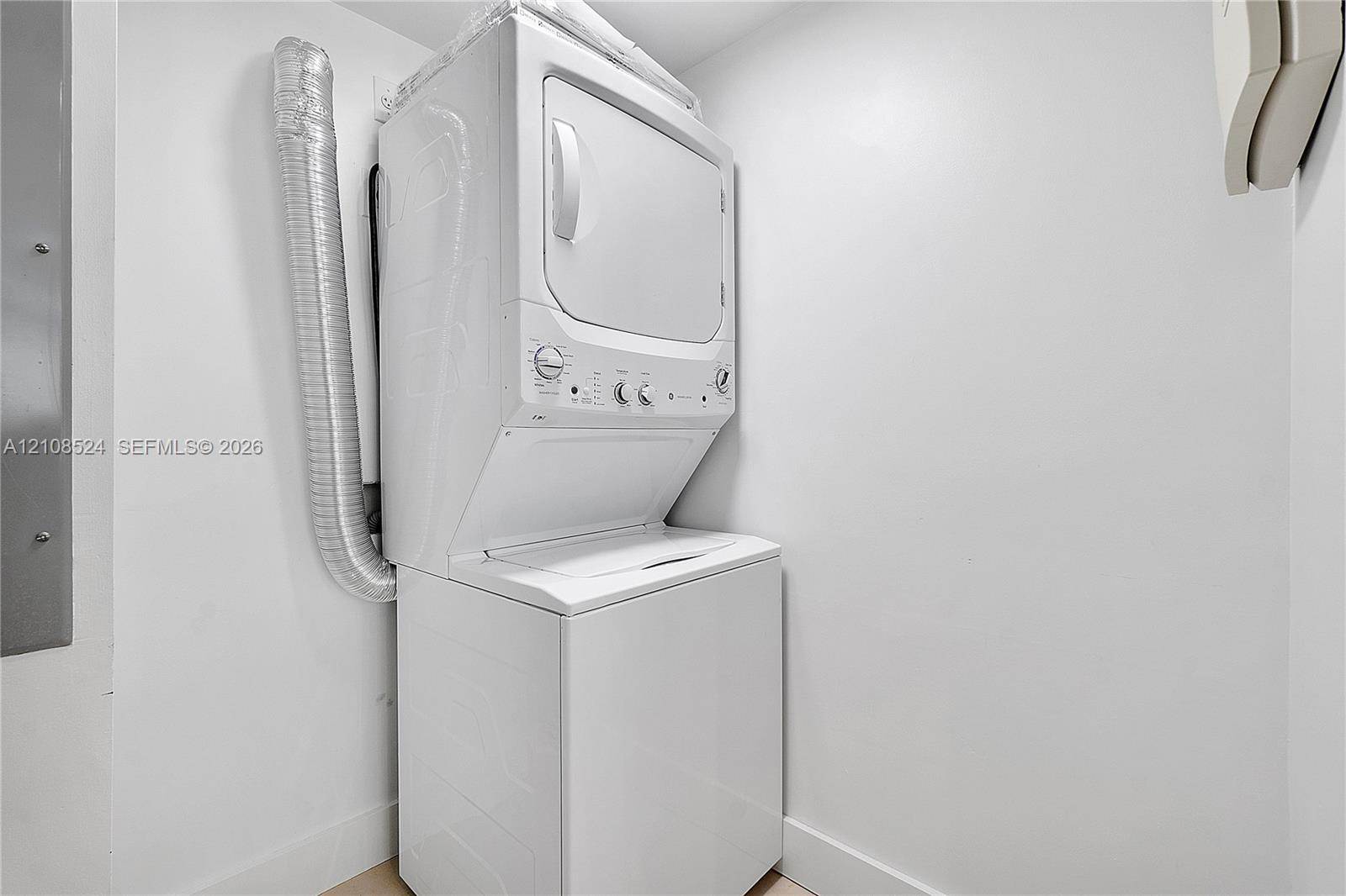 White stacked laundry unit featuring a top-loading washer, front-loading dryer, and metallic venting