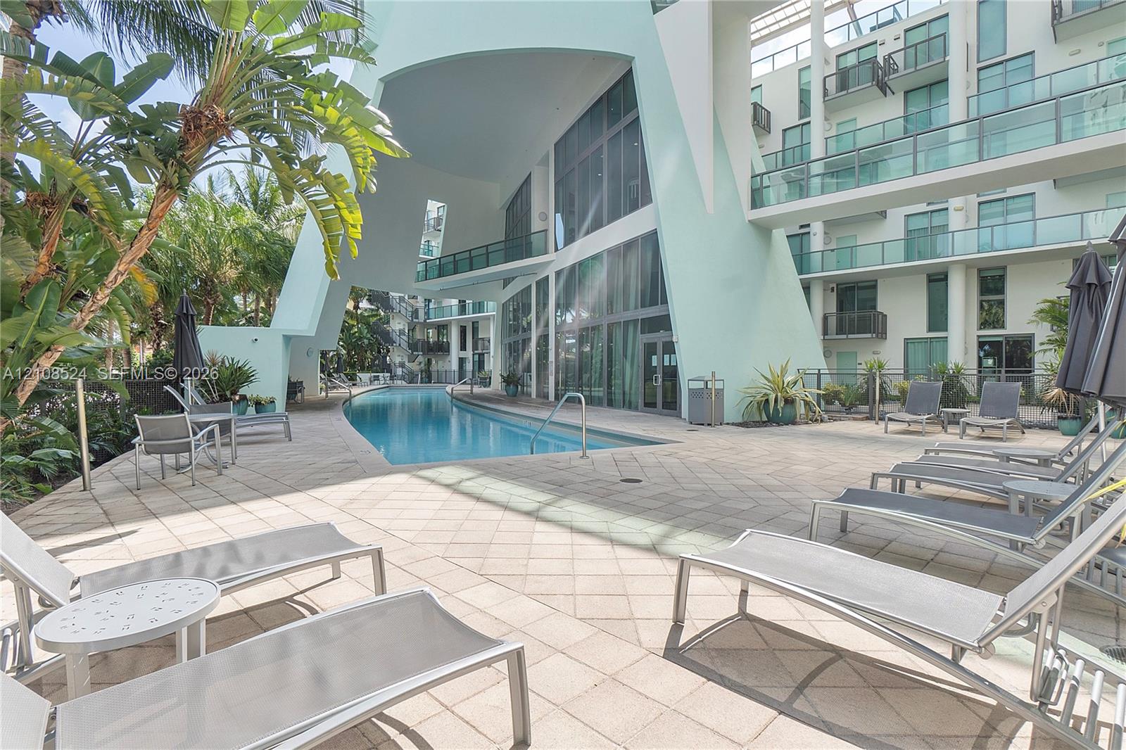 Swimming pool with a paved deck, towering architectural structure with floor-to-ceiling glass, and mature palms