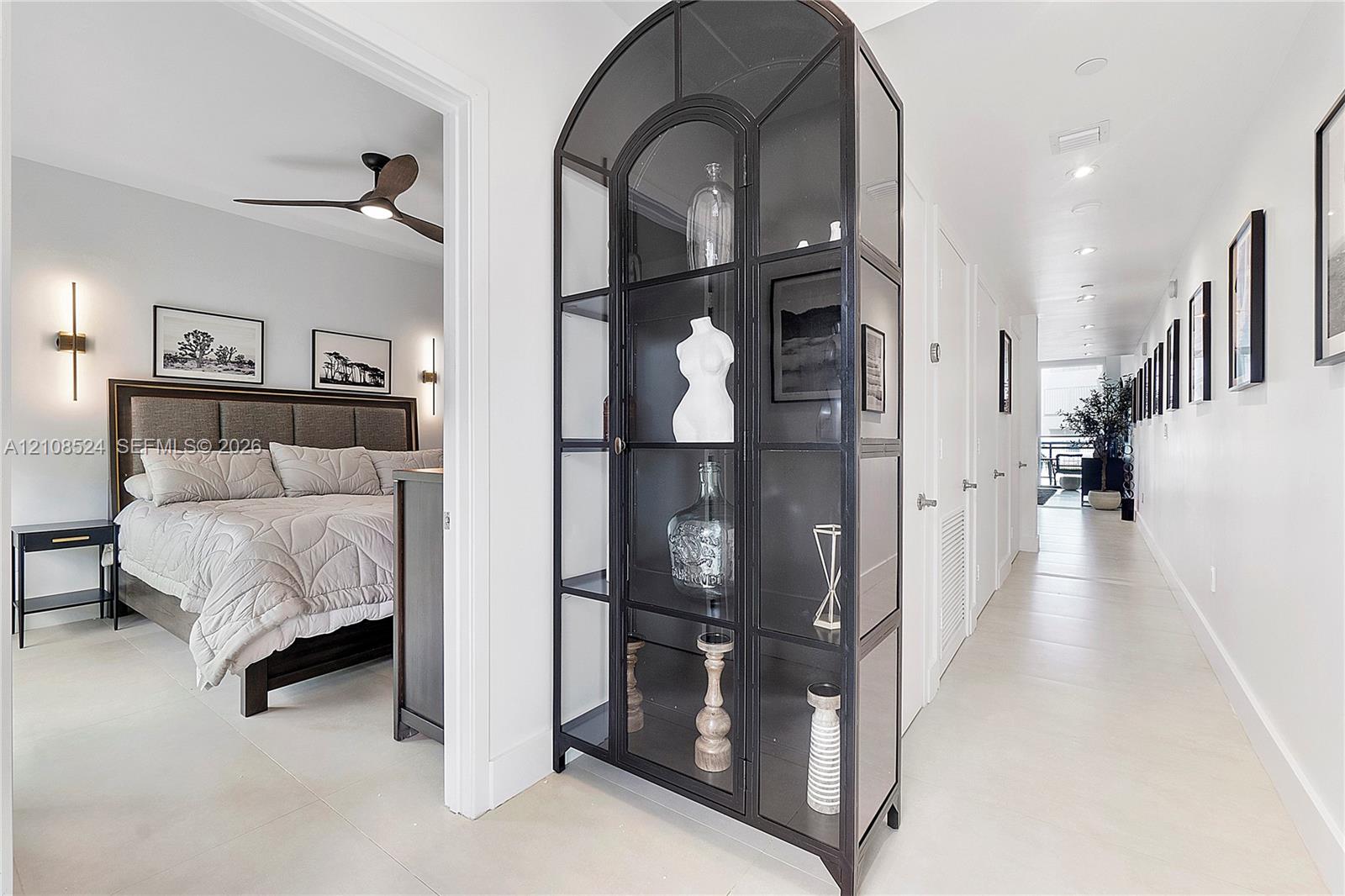 Hallway featuring large-format light-toned tile flooring, recessed ceiling lighting, and a built-in metal-framed glass display cabinet with an arched top Hallway featuring large-format light-toned tile flooring, recessed ceiling lighting, and a built-in metal-framed glass display cabinet with an arched top