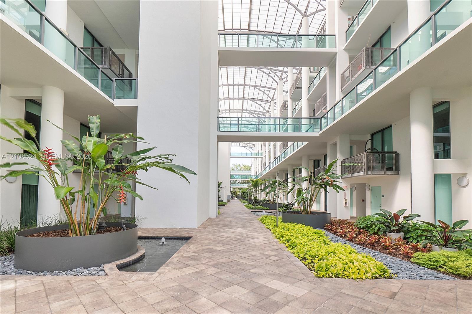 Atrium courtyard featuring a glass-paneled ceiling, stone-paved walkways, built-in circular metal planters, and structural walkways spanning multiple levels Atrium courtyard featuring a glass-paneled ceiling, stone-paved walkways, built-in circular metal planters, and structural walkways spanning multiple levels