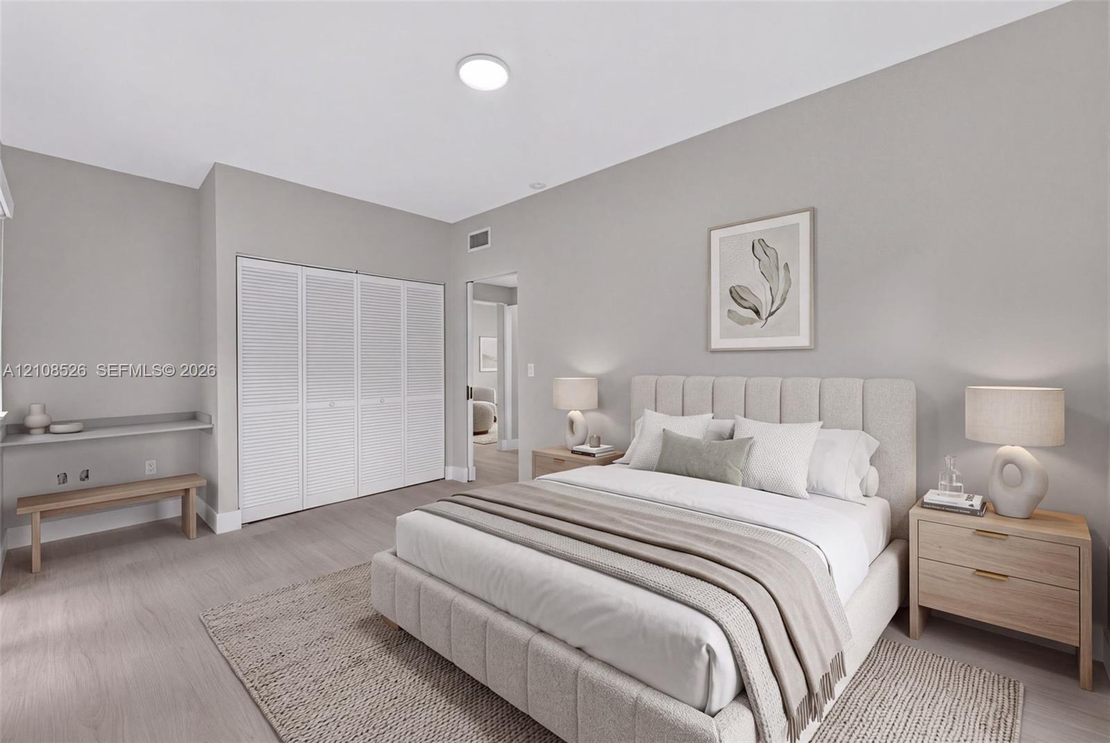 Neutral-toned interior space featuring light-toned wood-finish flooring, floor-to-ceiling white louvered closet doors, and a built-in floating desk surface