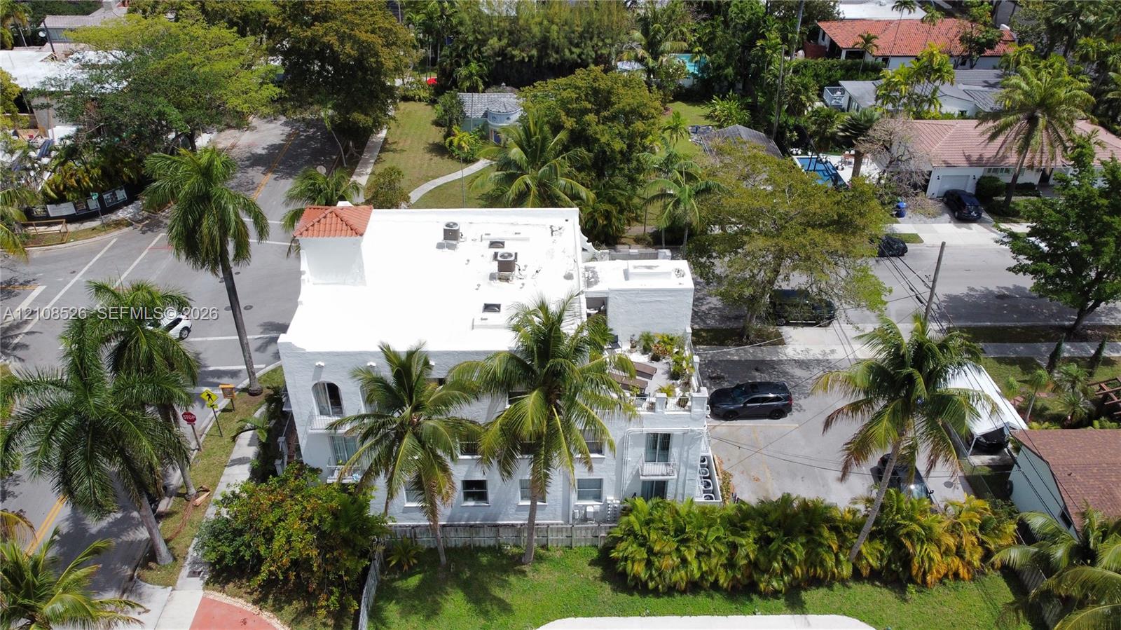 Multi-story building featuring a flat roof with parapet, exterior staircase, balcony levels, and mature landscaping