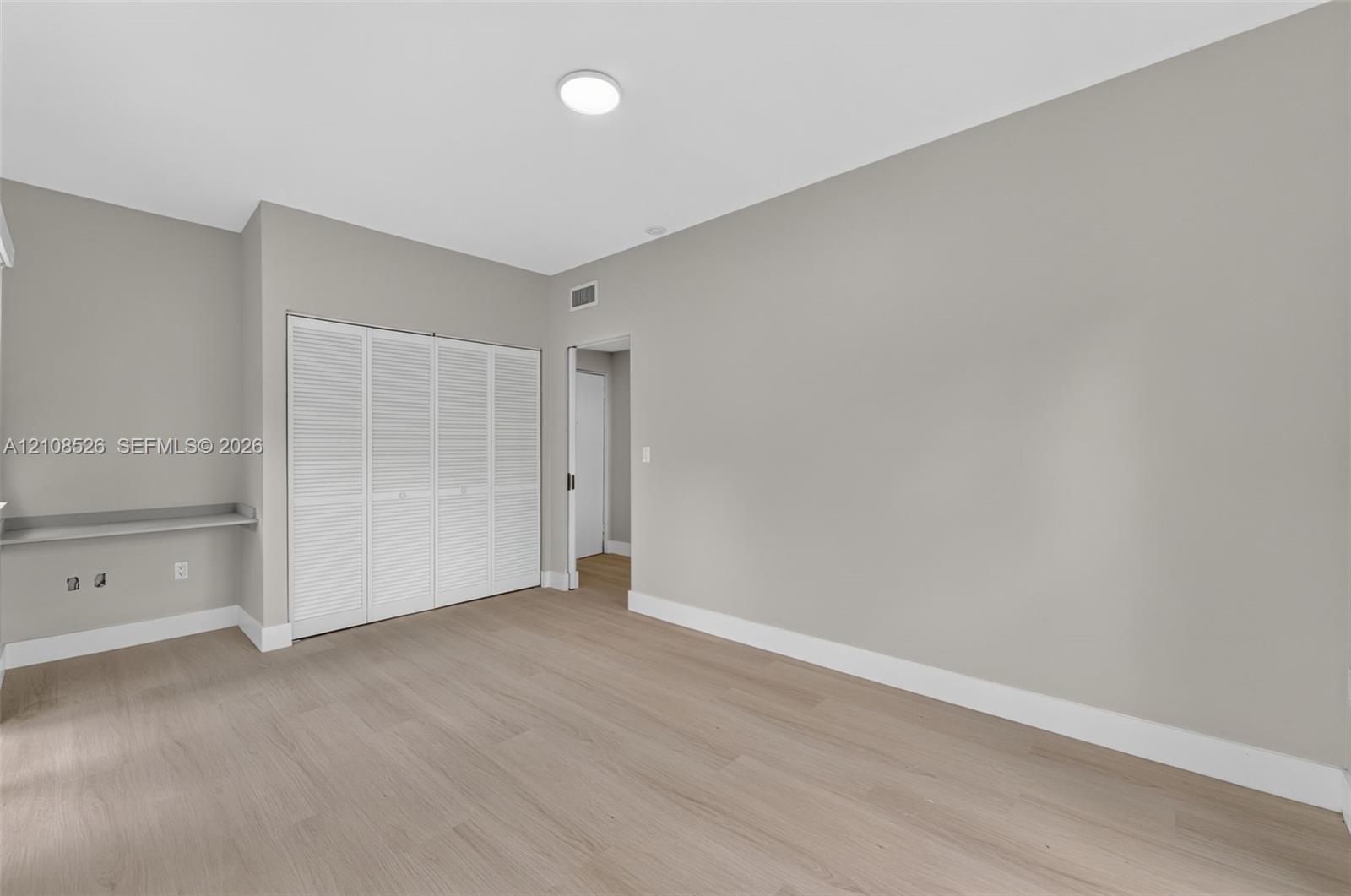 Neutral-toned interior space featuring wood-finish flooring, white louvered closet doors, and a built-in floating desk