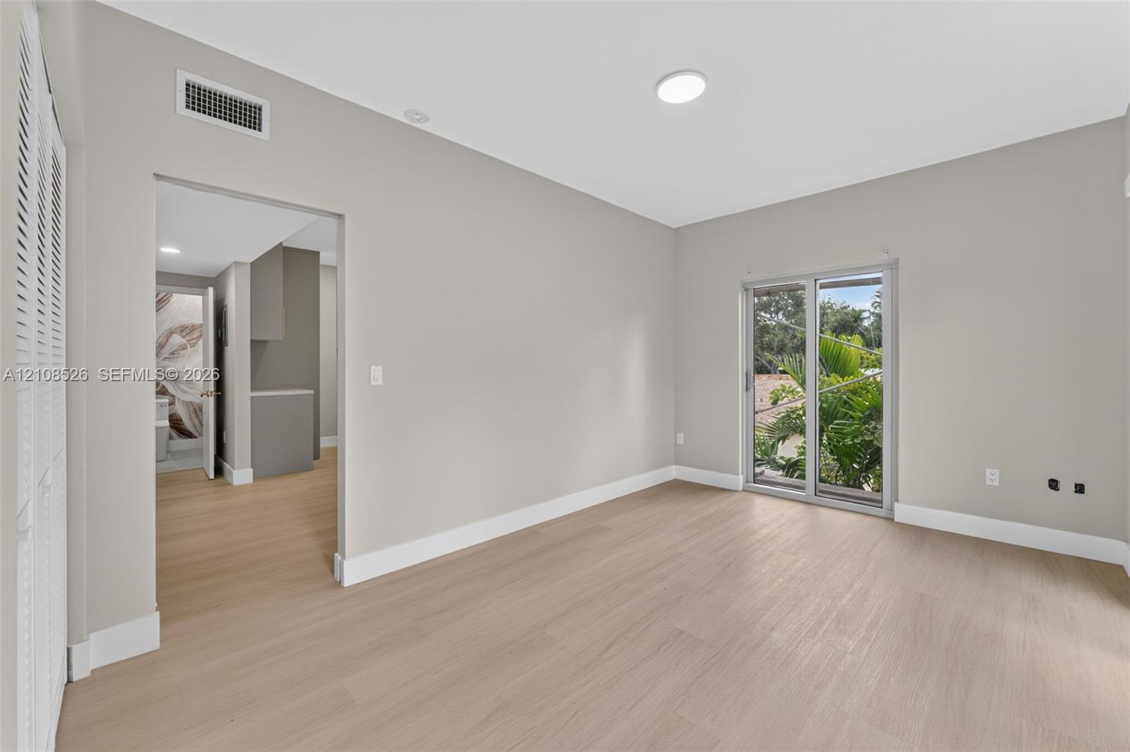 Neutral-toned interior featuring wood-finish flooring, sliding glass doors, and louvered closet doors