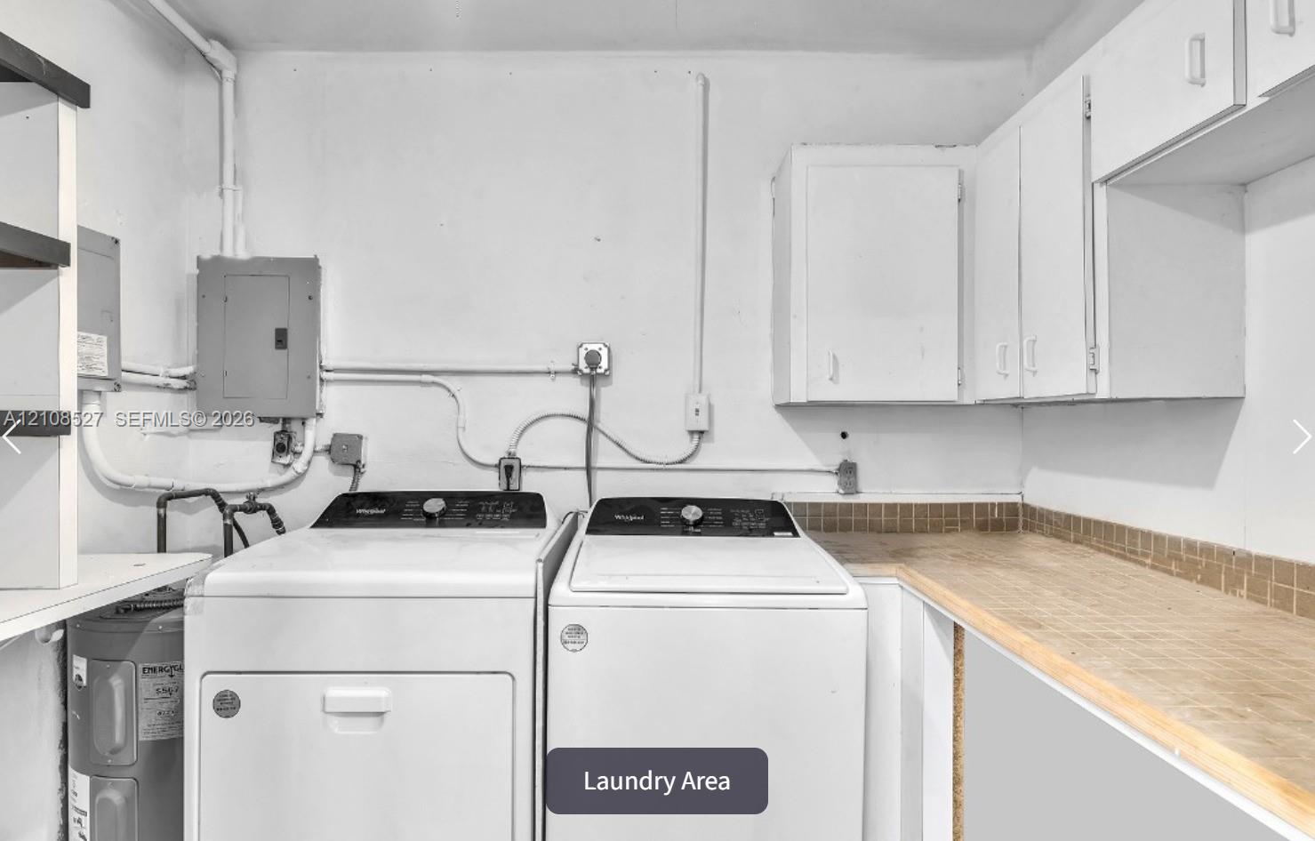 Laundry space featuring built-in white cabinetry, expansive wood-tone countertop, and tiled backsplash