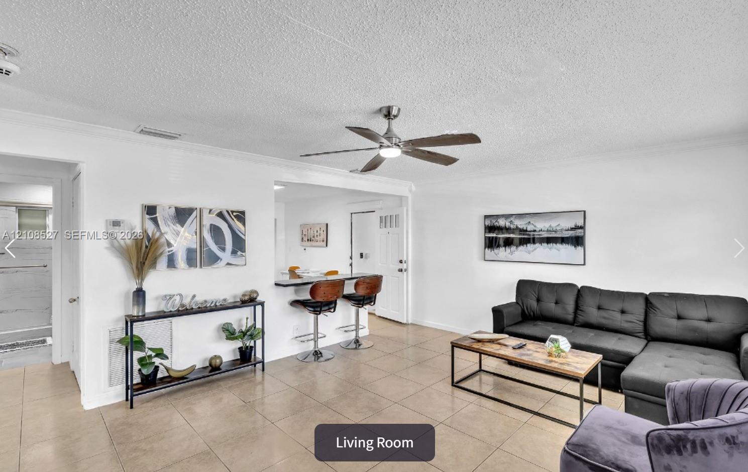 Open living area featuring large-format ceramic tile flooring, a neutral color palette, a brushed nickel ceiling fan, and a breakfast bar