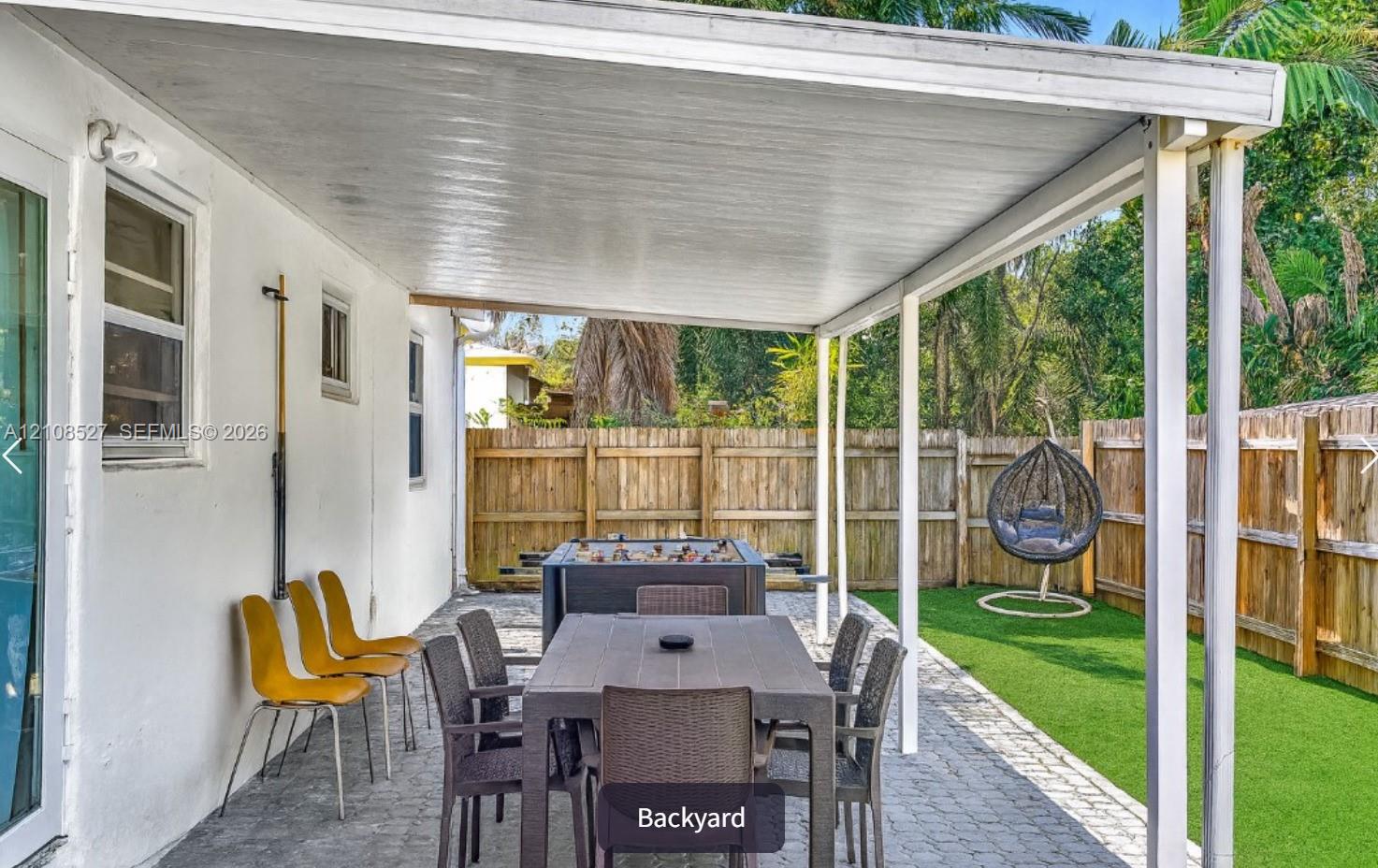 Covered outdoor patio with paver flooring, synthetic turf lawn, and wood privacy fencing