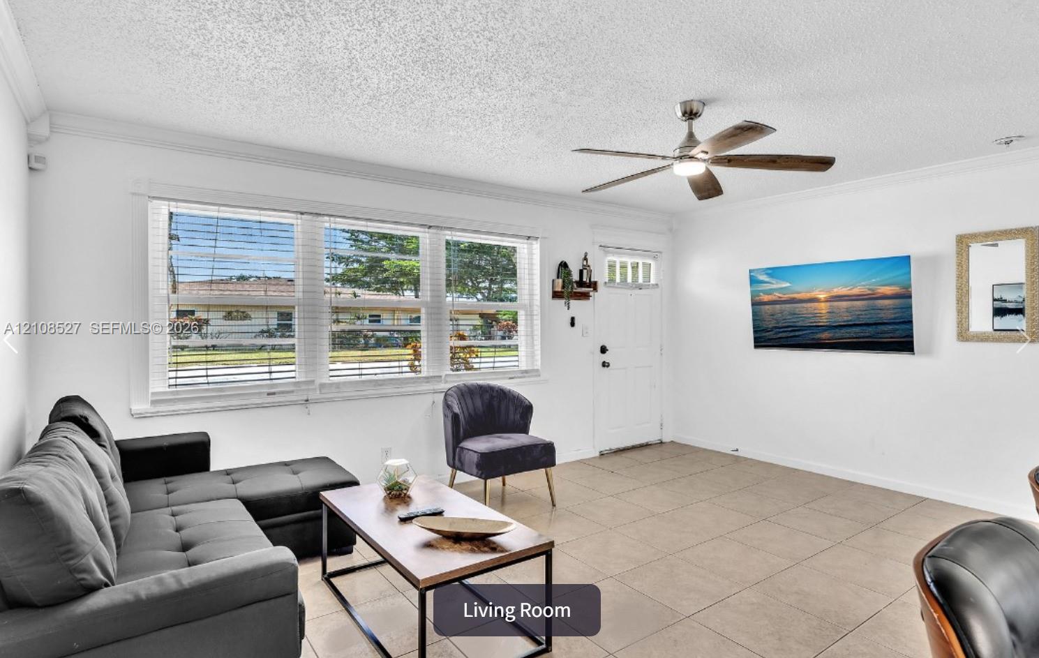 Living room featuring tile flooring, crown molding, large windows, and a ceiling fan with integrated light fixture