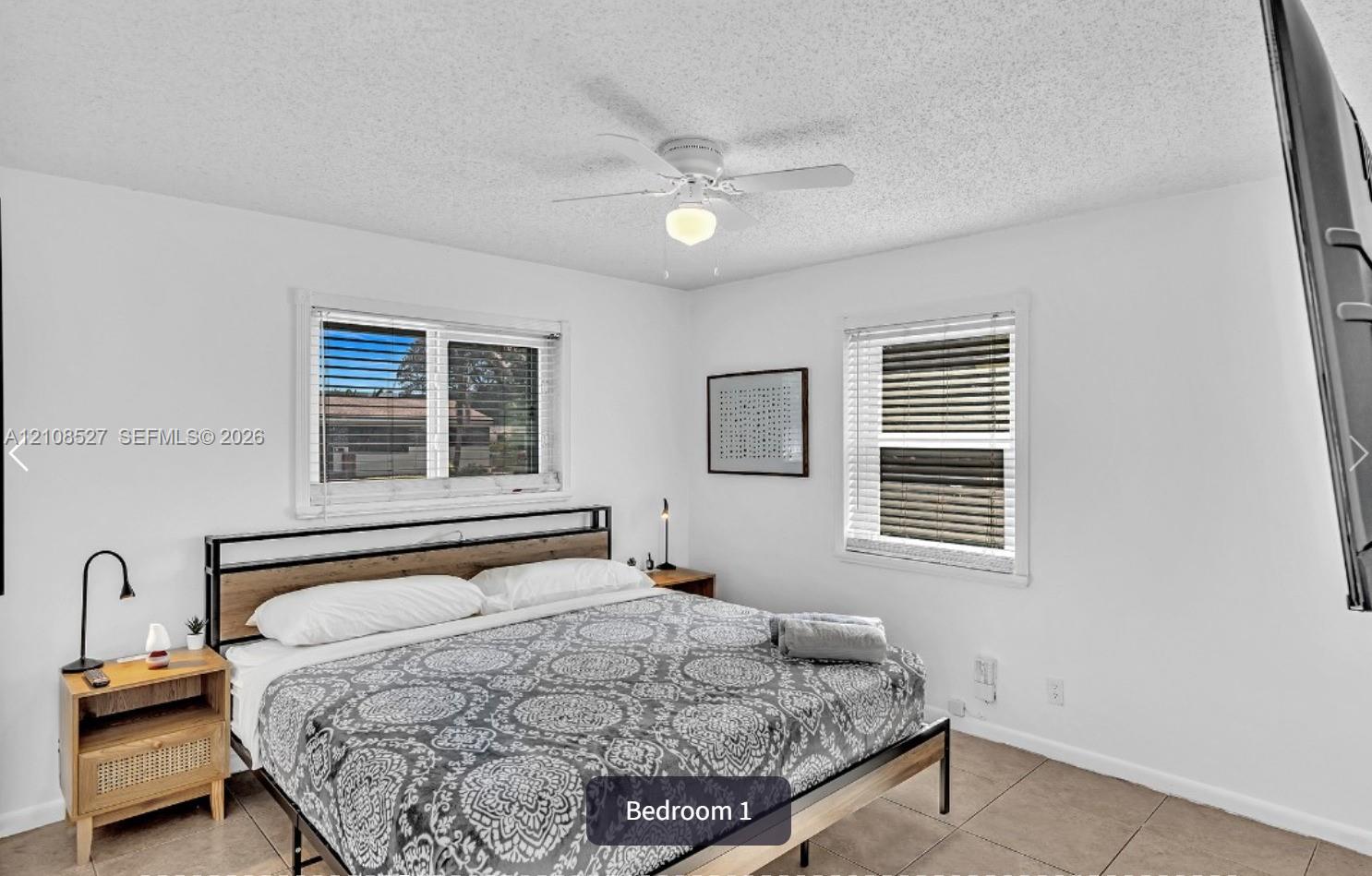 Neutral interior room featuring tile flooring, white walls, dual windows with integrated blinds, and a ceiling fan with light fixture