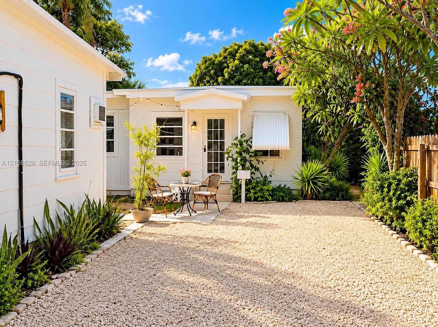 White horizontal siding exterior featuring a gravel courtyard, mature landscaping, and a glass-paneled entry door