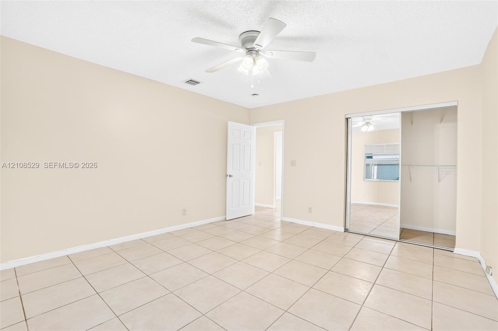 Interior space featuring neutral-toned tile flooring, a central ceiling fan with integrated lighting, and a closet with sliding mirrored doors