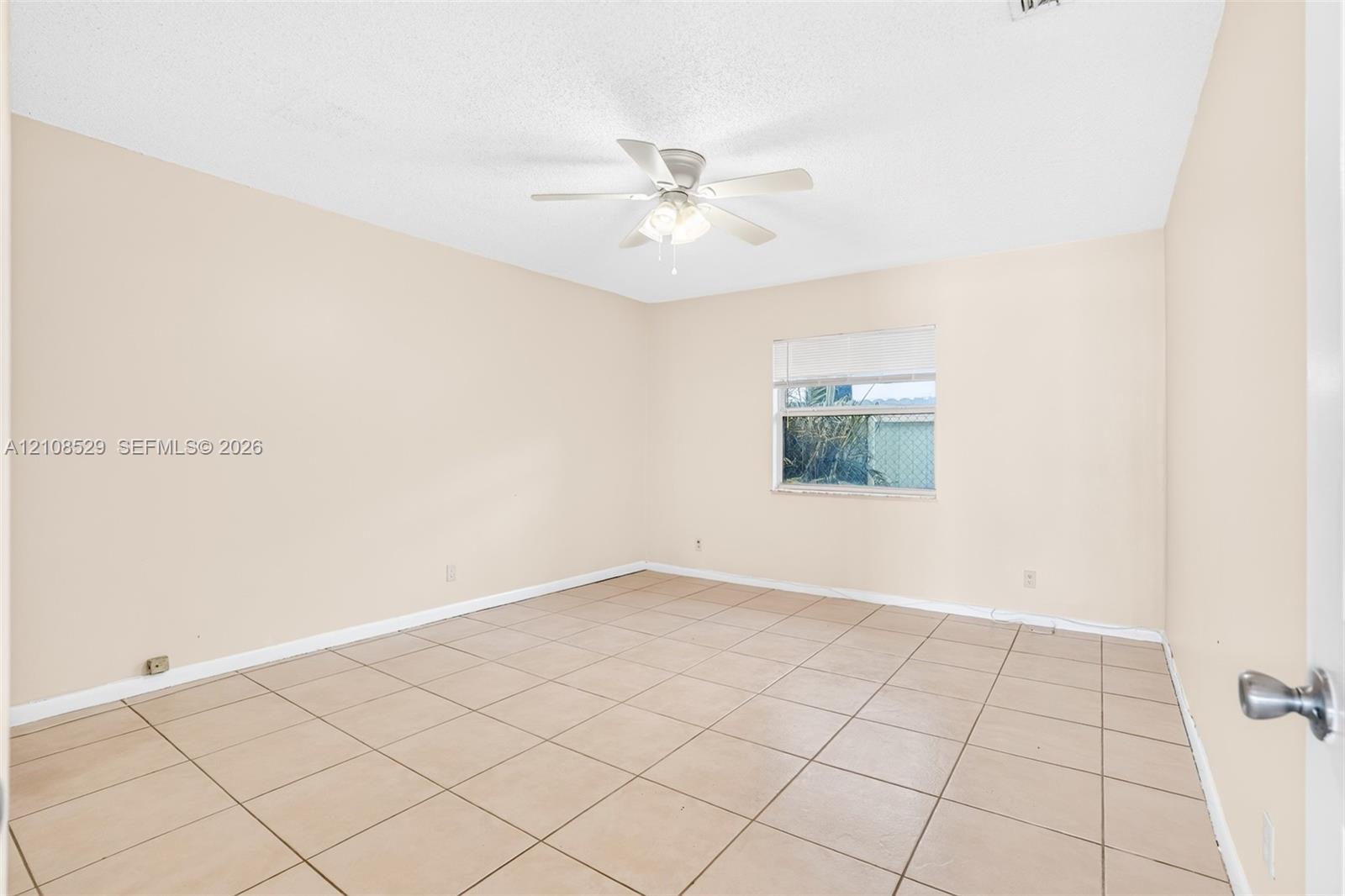 Neutral-toned interior space featuring ceramic tile flooring, a multi-blade ceiling fan with integrated lighting, and a single window with horizontal blinds
