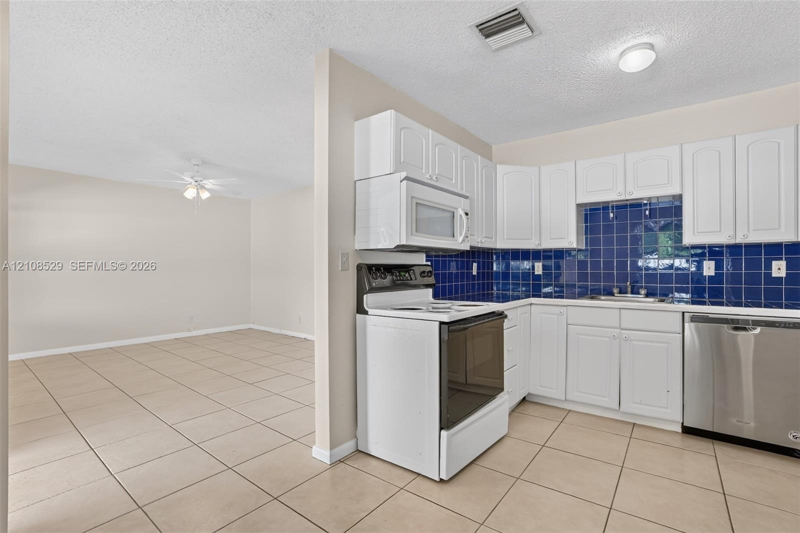 Kitchen featuring white cabinetry, blue tiled backsplash, stainless steel dishwasher, built-in microwave, and tile flooring