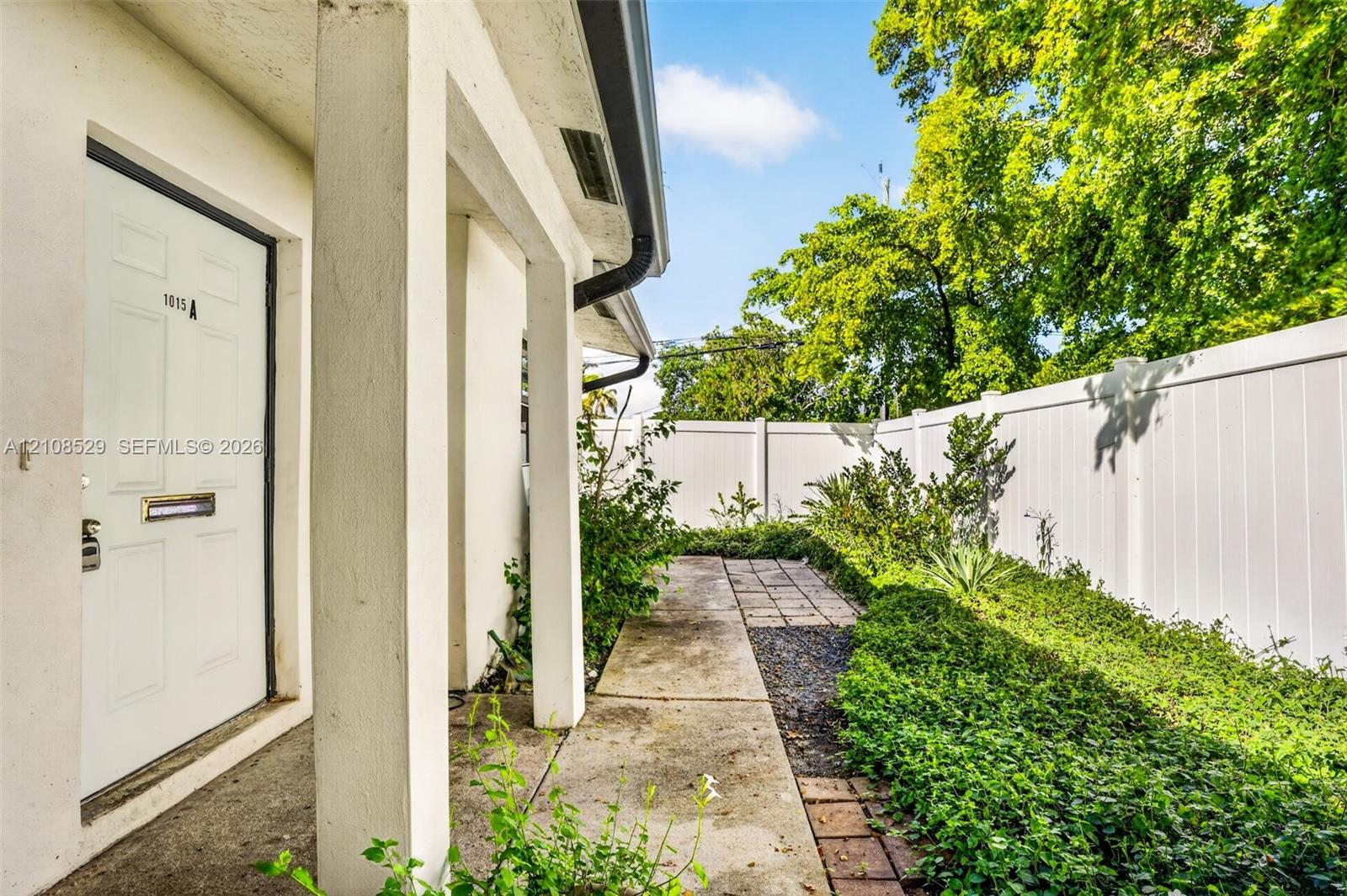 Covered entryway featuring structural pillars, concrete walkway, and white vinyl perimeter fencing