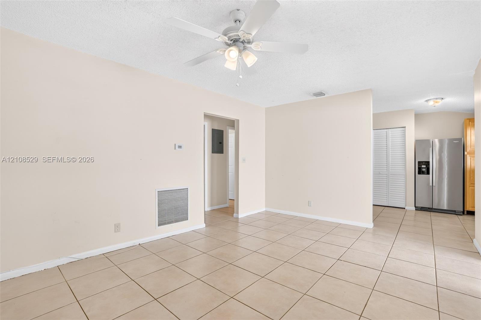 Open interior space featuring neutral tile flooring, a multi-light ceiling fan, and a stainless steel refrigerator