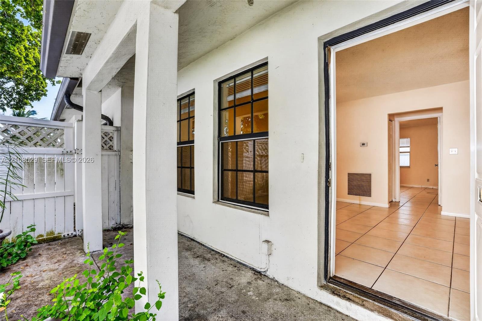 Covered exterior patio featuring a concrete floor, white structural columns, grid-patterned windows, and a white privacy fence
