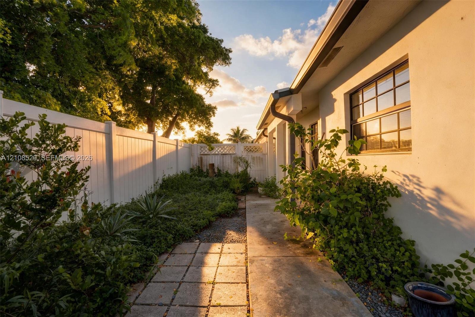 Exterior side yard featuring a concrete paver path, solid vinyl privacy fencing with lattice accents, multi-pane windows, and stucco siding