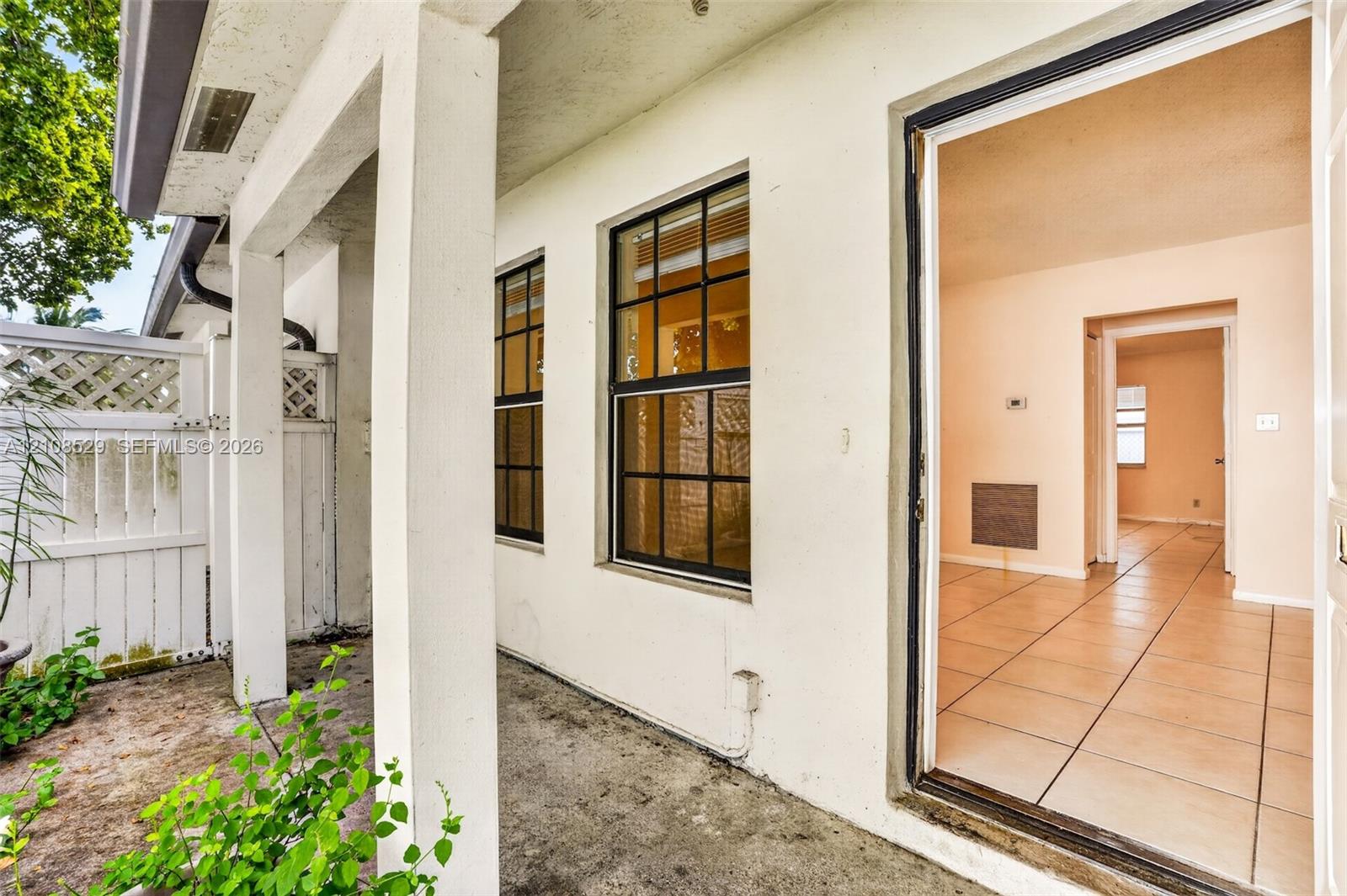 Covered patio featuring concrete flooring, white lattice privacy fencing, multi-pane windows with dark frames, and ceramic tile flooring throughout the interior Covered patio featuring concrete flooring, white lattice privacy fencing, multi-pane windows with dark frames, and ceramic tile flooring throughout the interior