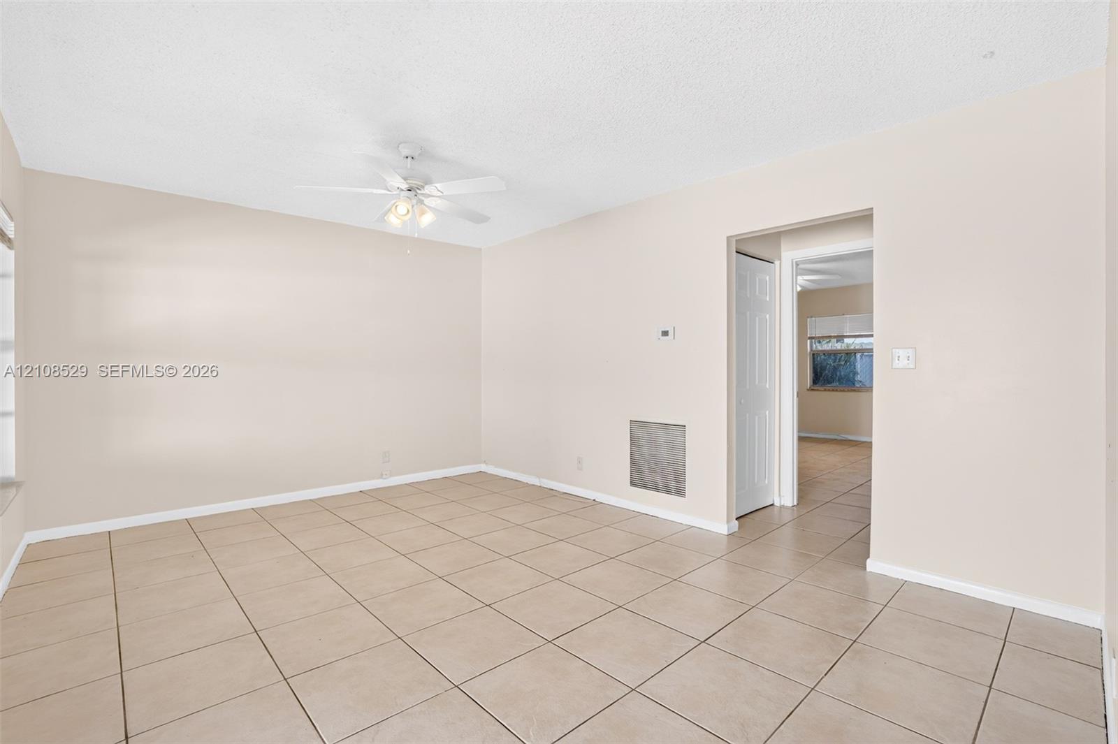 Neutral-toned interior featuring ceramic tile flooring, a white ceiling fan with integrated lighting, and a textured ceiling finish