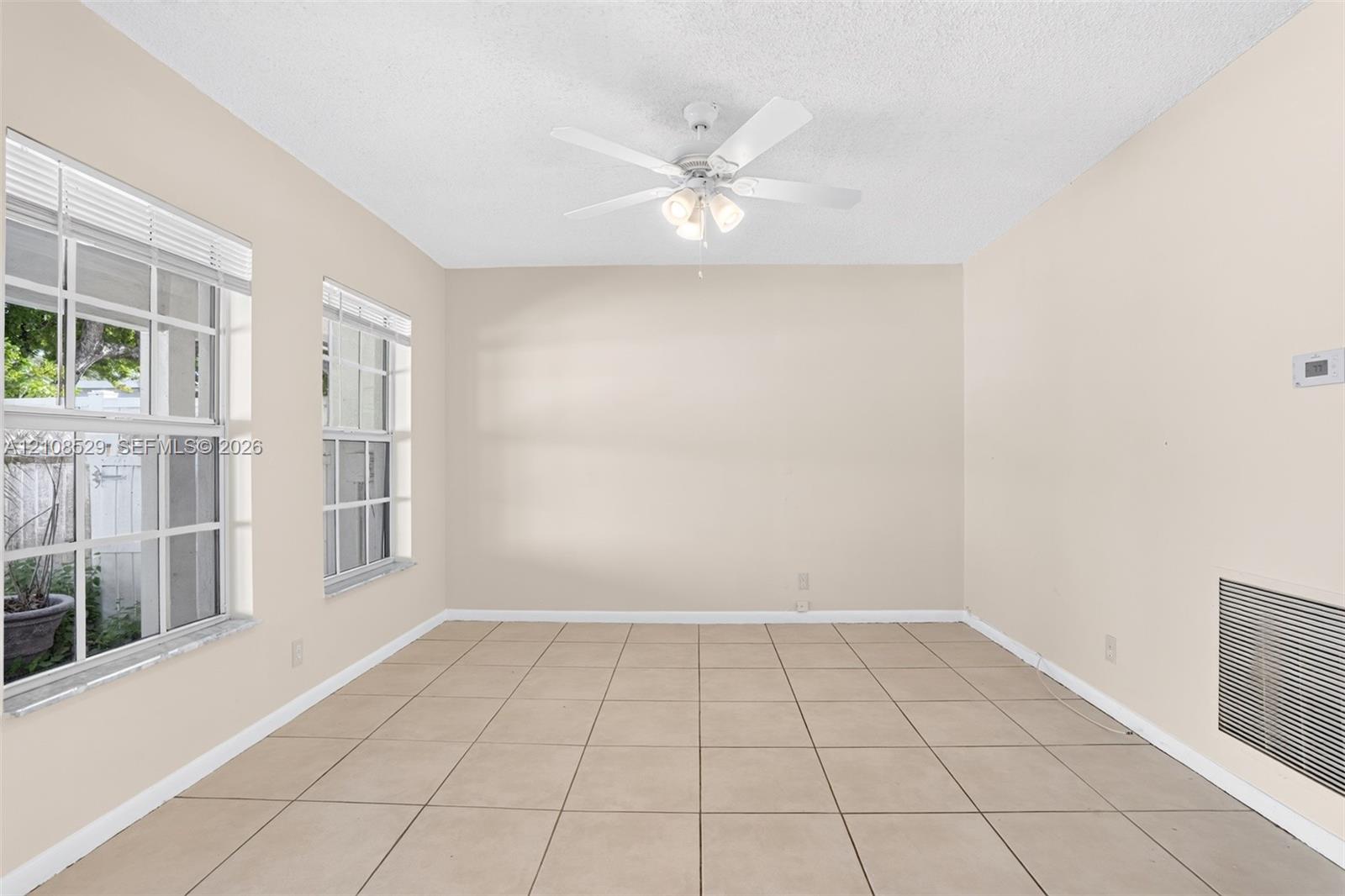 Interior space featuring large-format neutral floor tile, dual grid-pattern windows, and a ceiling-mounted light fixture with a multi-blade fan