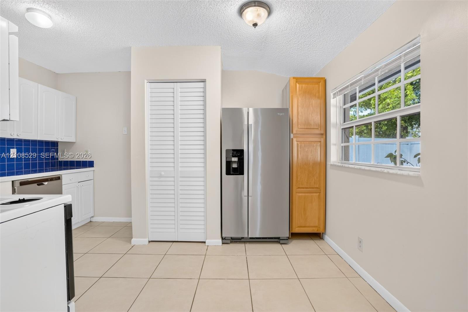 Kitchen featuring white cabinetry, blue tiled backsplash, stainless steel refrigerator, louvered closet doors, and ceramic tile flooring