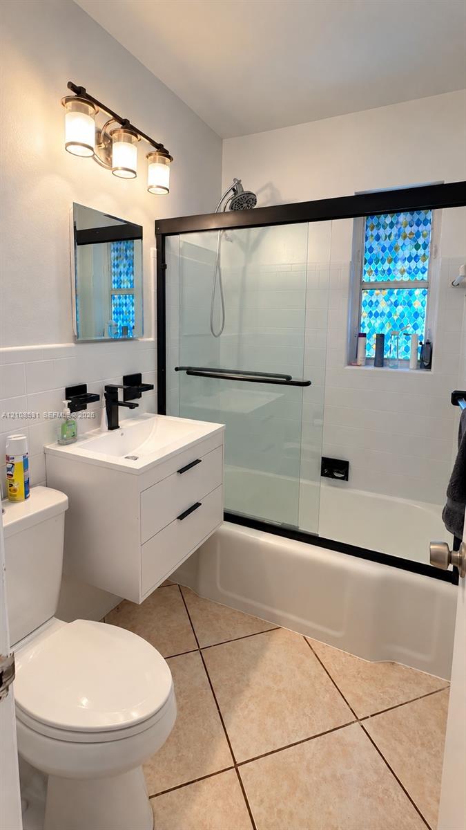 Floating white vanity with a rectangular sink, matte black faucet, wall-mounted three-light fixture, and sliding glass shower door with a black frame