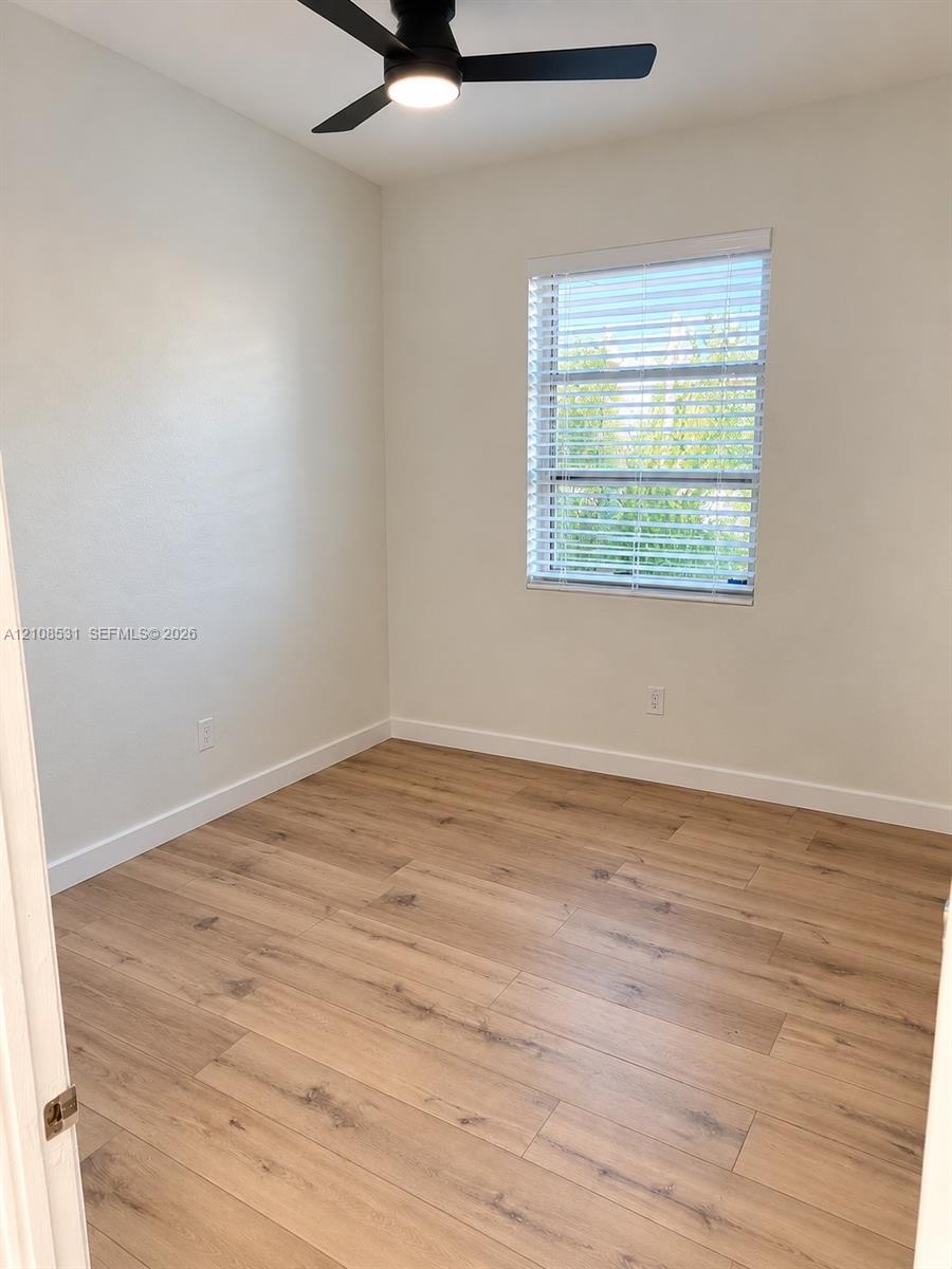 Room featuring wood-finish flooring, a matte black ceiling fan with integrated lighting, and a single-pane window with white horizontal blinds