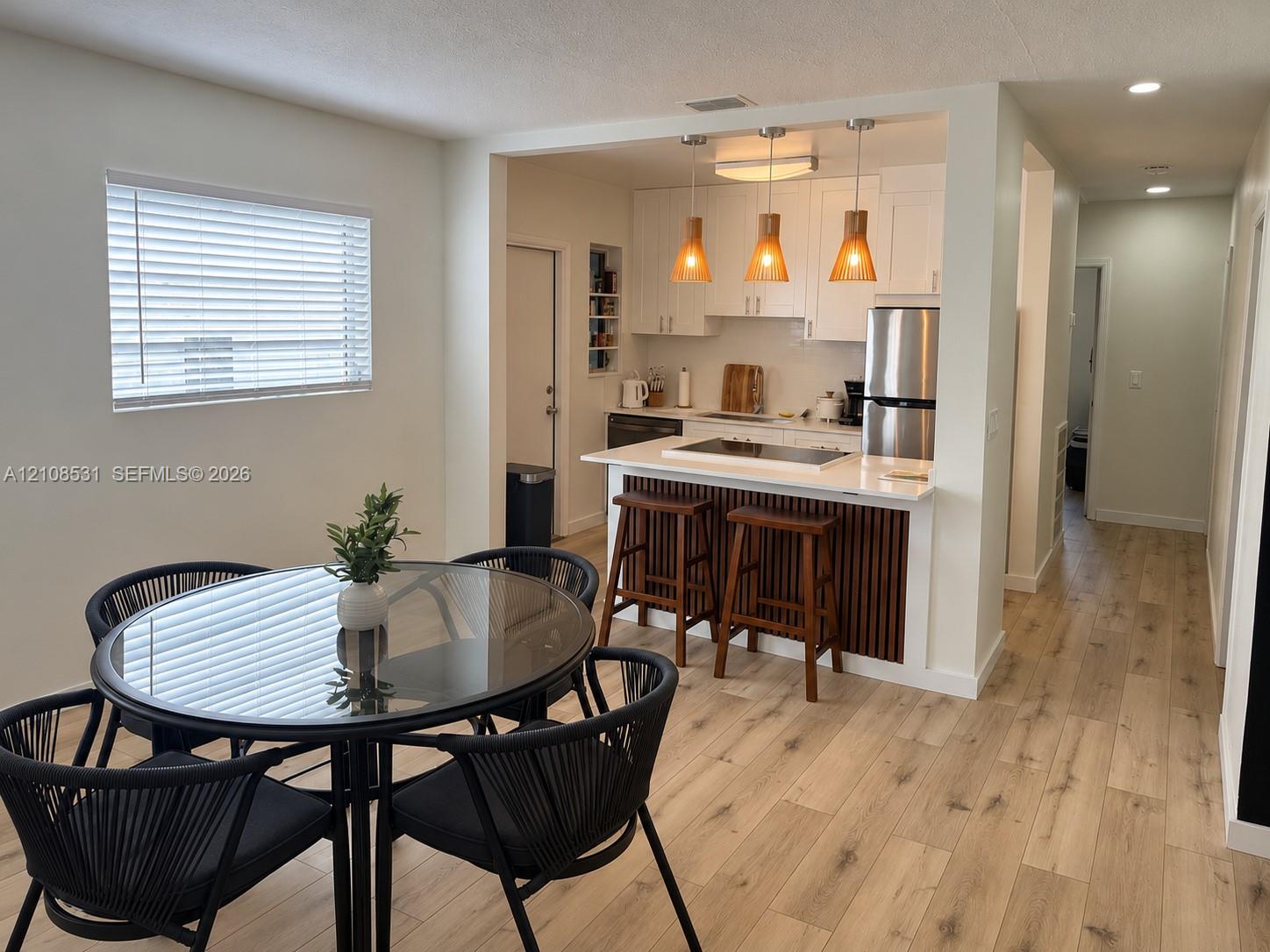 Kitchen featuring white shaker-style cabinetry, wood-slat peninsula detailing, quartz-surface countertops, stainless steel appliances, and wood-finish flooring throughout