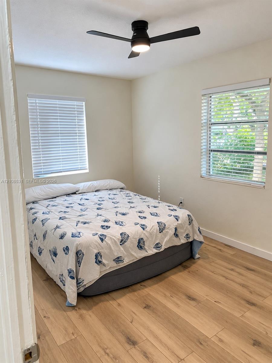 Neutral interior featuring light-tone wood-finish flooring, dual windows with horizontal blinds, and a modern matte black ceiling fan with integrated lighting