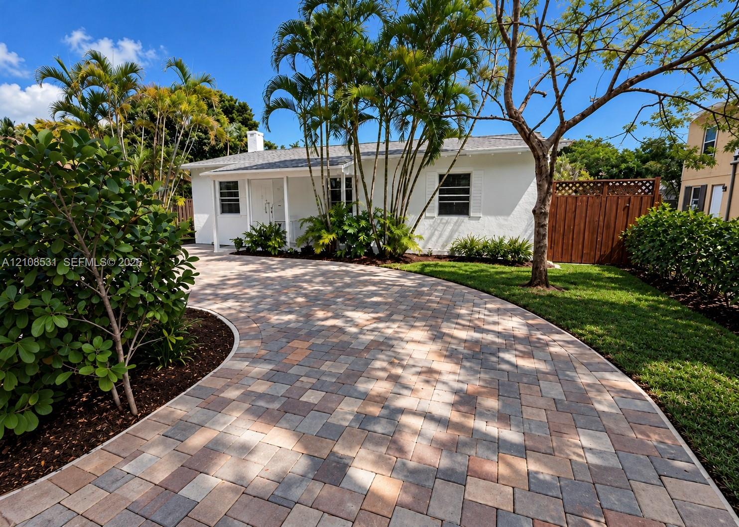 Single-story exterior featuring a multi-tone paver driveway, white stucco finish, front covered porch, and mature palm landscaping Single-story exterior featuring a multi-tone paver driveway, white stucco finish, front covered porch, and mature palm landscaping