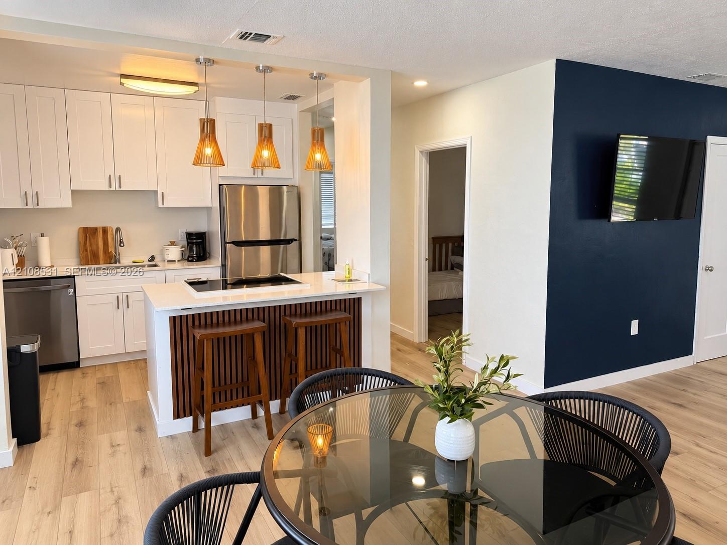 Kitchen featuring white cabinetry, quartz-surface countertops, stainless steel appliances, and a wood-slat breakfast bar accented by hanging pendant lighting