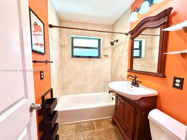 Bathroom featuring a vanity with an integrated basin, wall-mounted wooden-frame mirror, stone-tiled shower surround with decorative inlay, tile flooring, and three-light wall fixture