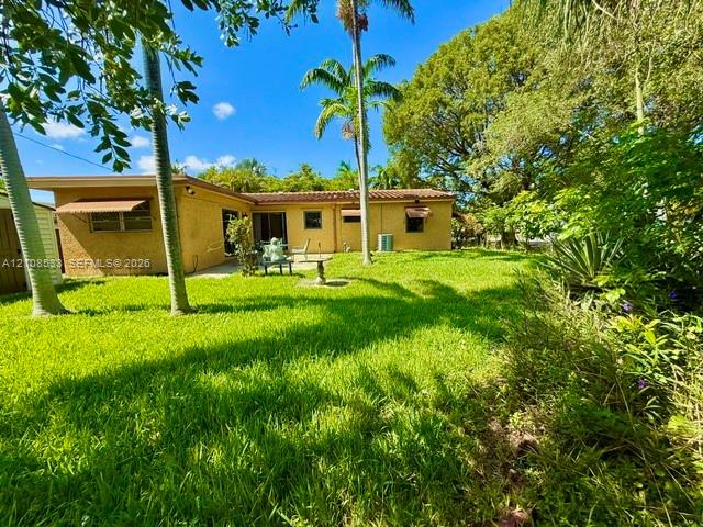 Rear exterior featuring a stucco facade, tile roof, concrete patio, and mature palm trees within a landscaped lawn
