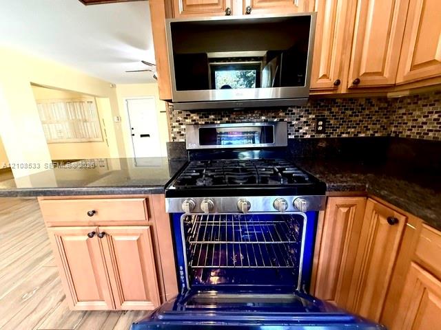 Kitchen featuring stained wood cabinetry, stone countertops, stainless steel gas range with convection oven, built-in microwave, and mosaic tile backsplash Kitchen featuring stained wood cabinetry, stone countertops, stainless steel gas range with convection oven, built-in microwave, and mosaic tile backsplash