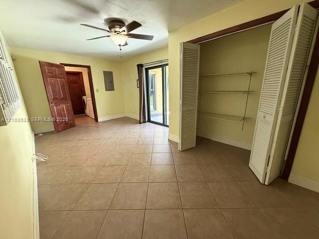 Room featuring square ceramic tile flooring, a ceiling fan with integrated lighting, bi-fold louvered closet doors with adjustable shelving, and a glass sliding door