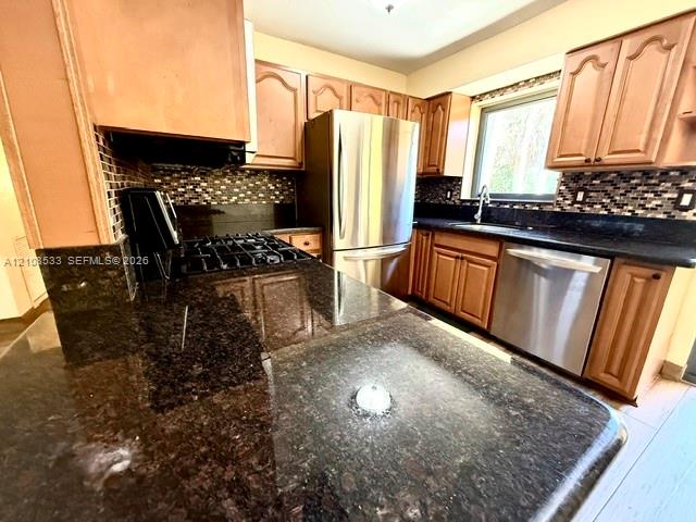 Kitchen featuring natural wood cabinetry, stone countertops, mosaic tile backsplash, and stainless steel appliances Kitchen featuring natural wood cabinetry, stone countertops, mosaic tile backsplash, and stainless steel appliances