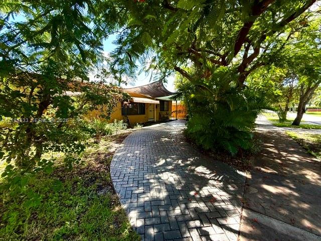 Paved brick driveway featuring a fabric shade structure and established mature trees