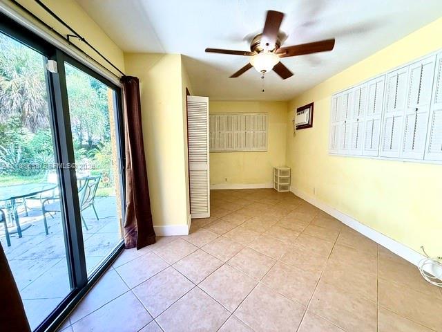 Sunroom featuring tile flooring, sliding glass doors, white louvered shutters, and a ceiling fan