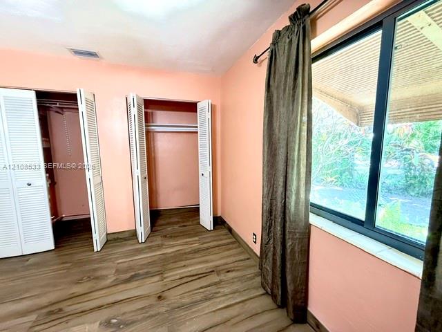 Room featuring wood-finish flooring, dual closets with louvered doors, and a large window with a stone sill