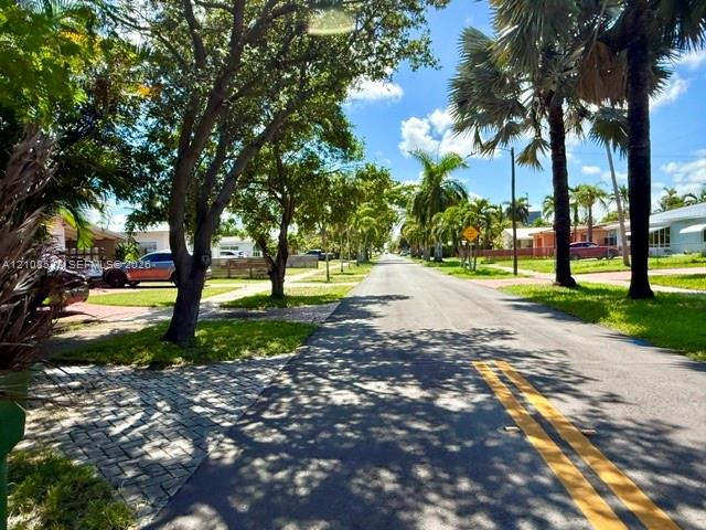 Paved streetscape featuring mature palm trees, established shade trees, and paver stone driveway accents