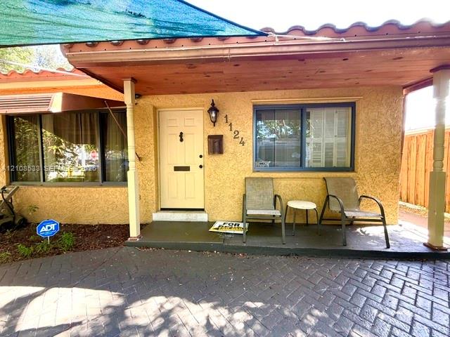 Stucco exterior entry featuring a covered porch, herringbone-patterned brick paver driveway, solid-core front door, and mission-style roof tiles