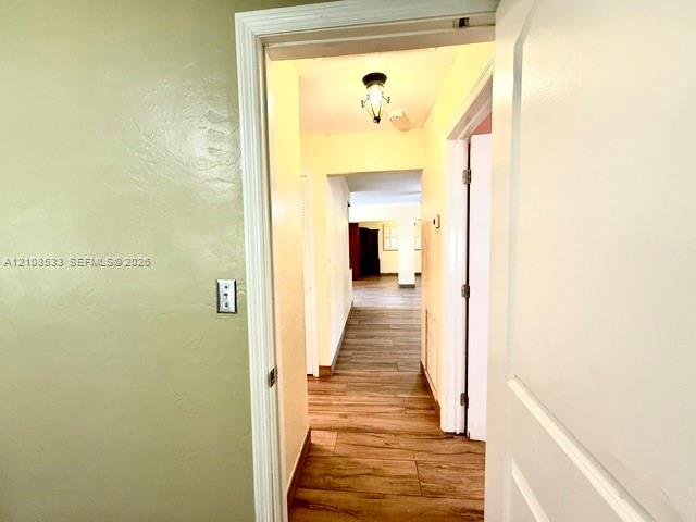 Interior hallway featuring wood-finish flooring, textured walls, and a decorative flush-mount ceiling fixture