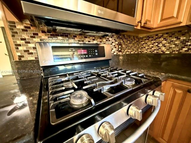 Stainless steel gas range with a built-in microwave, dark stone countertops, mosaic tile backsplash, and wood-finish cabinetry Stainless steel gas range with a built-in microwave, dark stone countertops, mosaic tile backsplash, and wood-finish cabinetry