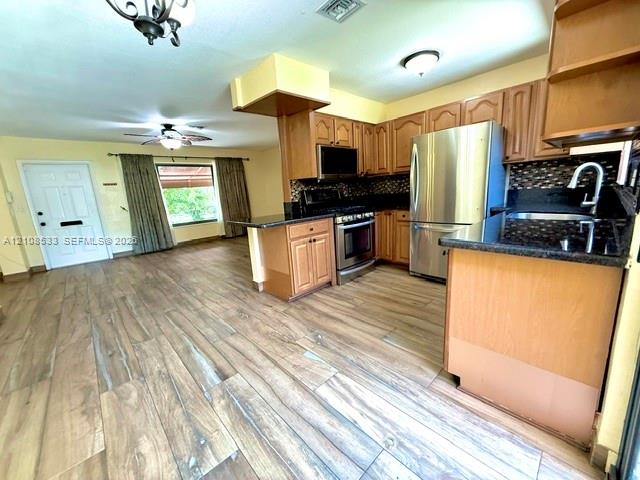 Kitchen featuring wood-finish flooring, stainless steel appliances, dark stone-composite countertops, and wood cabinetry Kitchen featuring wood-finish flooring, stainless steel appliances, dark stone-composite countertops, and wood cabinetry